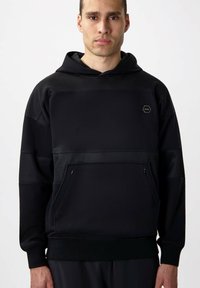 Sudadera con capucha negra que presenta un panel superior texturizado, un bolsillo tipo canguro en la parte delantera y puños acanalados. Logo notable en forma hexagonal en el pecho.
