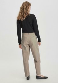 Beige op maat gemaakte broek met een hoge taille en zijzakken, gecombineerd met een zwart lang-leeve top, met een ontspannende pasvorm en een gestructureerde stof.
