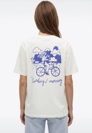Person with long hair wearing white shirt featuring blue graphic of cyclist in mountains with clouds and "Sunday morning" text on back.