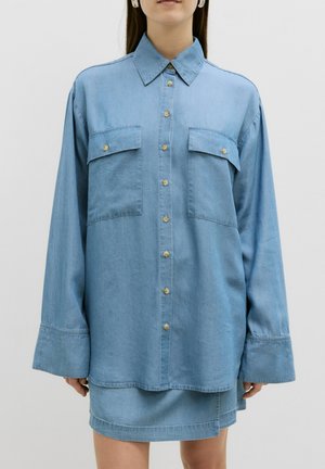 Lichtblauw denim shirt met een puntige kraag, twee borstzakken en knoopsluiting. Heeft lange mouwen en een ontspannen pasvorm.