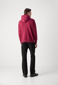 Felpa con cappuccio in rosa scuro, con cappuccio regolabile, vestibilità comoda e polsini a coste, abbinata a pantaloni neri a gamba dritta e scarpe.