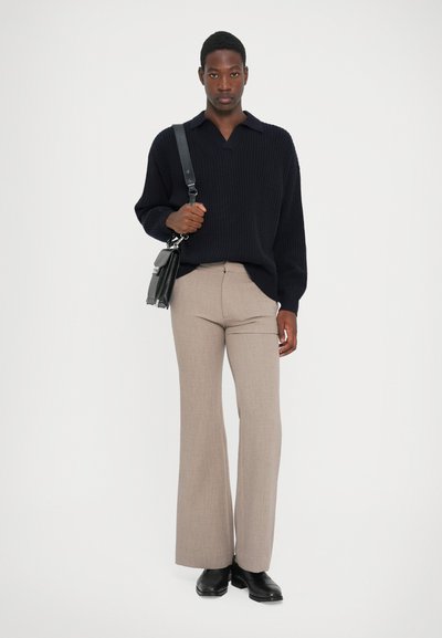 Navy knitted sweater with a collar, beige flared trousers, and black leather ankle boots. Model holds a black crossbody bag.