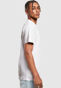 White cotton T-shirt with short sleeves, regular fit, and crew neckline. Model has braided hair and is wearing light blue jeans.
