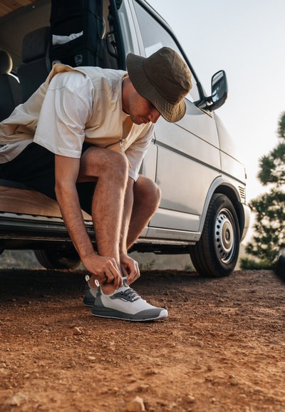 Grey and white sneaker with a running shoe design, flexible upper material, rubber sole, and lacing system, worn by a person.