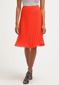 Röd plisserad kjol gjord av lättviktsmaterial, med en utsvängd form och slät yta. Bärs med en randig topp och svarta sandaler.