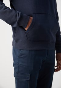 Sudadera de algodón azul marino con un bolsillo frontal, puños y dobladillo acanalados. Combinada con pantalones cargo azul marino que cuentan con bolsillos laterales y una textura suave.
