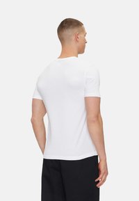 Camiseta blanca de algodón de manga corta y cuello redondo, con una textura suave y un diseño sencillo, combinada con pantalones negros.