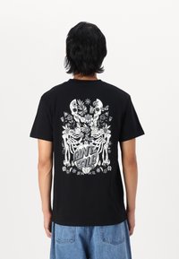Black cotton t-shirt featuring a large white graphic design of skeletons surrounded by flowers on the back. Crew neck, short sleeves.