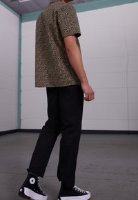 Koszula z krótkim rękawem w panterkę w odcieniach beżu i czerni, zestawiona z czarnymi spodniami i czarnymi wysokimi trampkami z białymi akcentami.