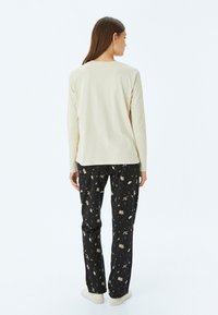 Beige lange mouwen top, gecombineerd met zwarte pyjamabroek met een patroonontwerp, inclusief verschillende iconen en lichtgewicht materiaal.