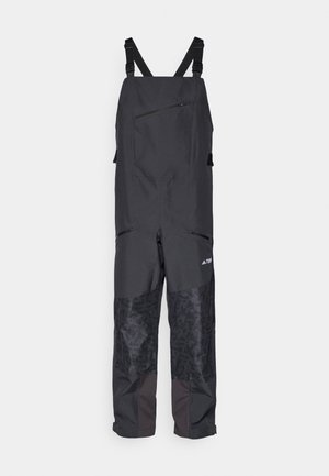 Schwarze wasserdichte Latzhose mit verstellbaren Trägern, einer Reißverschlusstasche und strukturierten Stoffakzenten an den Unterschenkeln.