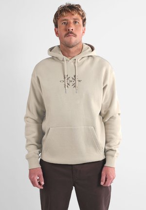 Sweat à capuche beige avec une poche kangourou à l'avant, une capuche à cordon de serrage et un logo discret en texte foncé. Tissu doux, coupe décontractée et poignets côtelés.