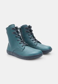 Un paio di stivali ankle in pelle teal con lacci neri, cerniere laterali e suole in gomma piatte su uno sfondo bianco.