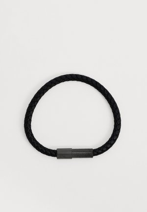 Sort flet læderarmbånd med en cylindrisk metal lukning på en ensartet lys baggrund.