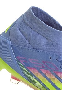 Blue athletic shoe with a high ankle collar, gradient pink and green accents, textured surface, and prominent stylized branding.