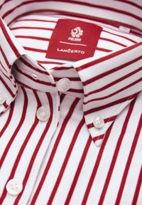 Biała koszula z czerwonymi pionowymi paskami i kołnierzykiem na guziki, z czerwoną metką wewnątrz kołnierzyka z napisem "POLSKA" i "LANCERTO."