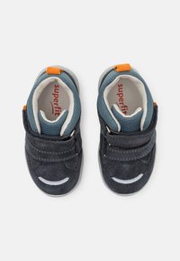 Mėlynos suede batukai mažyliams su lipduku, pilku guminio pado, baltais akcentais ir oranžiniu akcentu ant kulno. Sukurta komfortui ir atramai.