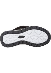Semelle noire avec un motif de bandage blanc, présentant une surface texturée et des points de traction triangulaires. Mesure environ 28 centimètres de long.