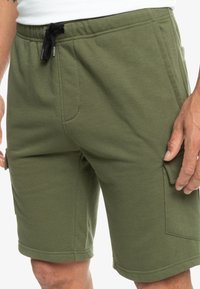 Olivově zelené bavlněné kraťasy s nastavitelným páskem, bočními kapsami a kapsou typu cargo. Hladká textura a délka do kolen.