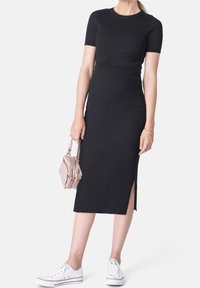 Mustassa ribatulla midi-mekolla, jossa on lyhyet hihat ja sivureikä, yhdistetty valkoisiin lenkkareihin ja pieneen vaaleanpunaiseen käsilaukkuun.