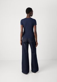 Mørkeblå t-skjorte med korte ermer, kombinert med brede, mørke jeans, med klassisk snitt og en ren finish uten mye pynt.