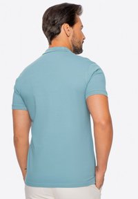 Koszulka polo wykonana z miękkiego niebieskiego materiału, z krótkimi rękawami, żeberkowym kołnierzykiem i klasycznym krojem. Charakteryzuje się teksturowaną powierzchnią z minimalnymi detalami w szwach.