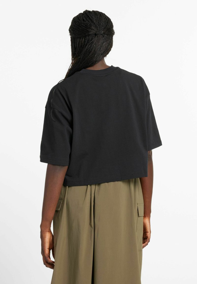 Cropped black cotton t-shirt with short sleeves, round neckline, and relaxed fit, paired with an olive green, pleated skirt featuring pockets.