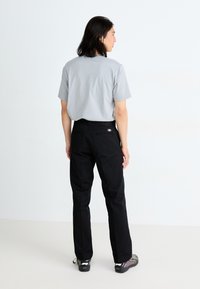Tricou gri cu mânecă scurtă, pantaloni negri cu buzunare în spate și încălțăminte închisă la culoare. Design minimalist și culori uni, văzute din spate.