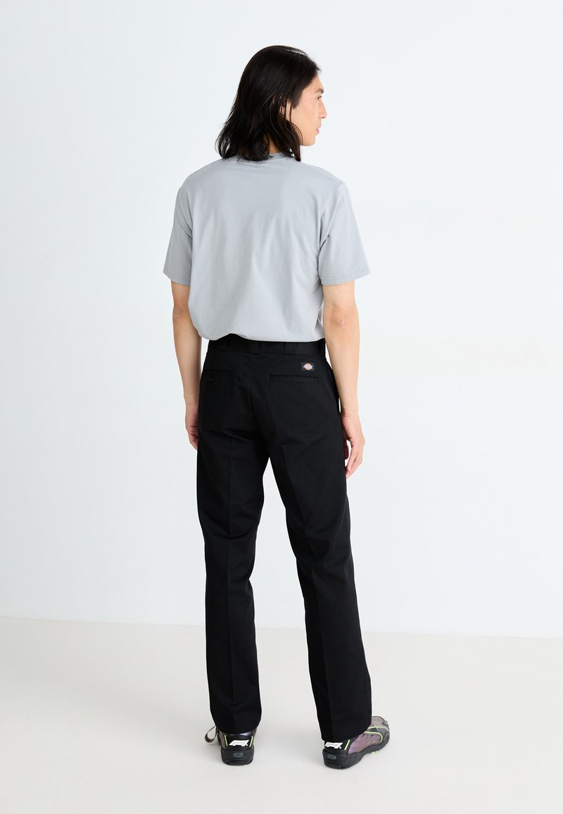 Graues T-Shirt mit kurzen Ärmeln, schwarze Hosen mit Gesäßtaschen und dunkle Schuhe. Minimalistisches Design und einfarbige Farben, von hinten betrachtet.