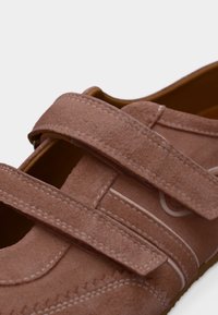 Απαλή καφέ σουέτ παπούτσι με δύο πλαίες λουρίδες βέλκρο και λευκές λεπτομέρειες ραφής.