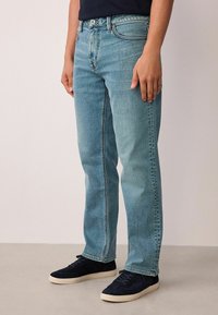 Világoskék farmer egyenes szabással, ötpocketes kialakítással, kontrasztos varrással és fakó hatással. Sötétkék velúr tornacipővel viselve.