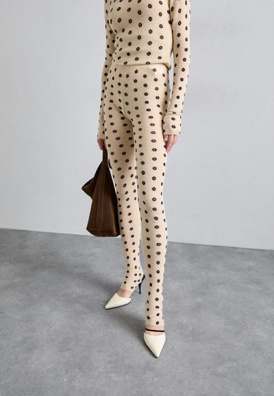 Set in maglia a costine beige con motivi floreali neri, leggings aderenti, maniche lunghe e una borsa a tracolla marrone; abbinato a tacchi bianchi a punta.