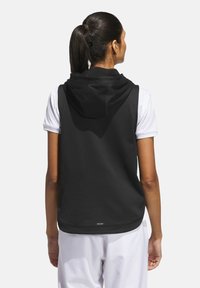 Black sleeveless hoodie with a soft texture and a large hood, worn over a white short-sleeve shirt. Features a subtle logo at the hem.