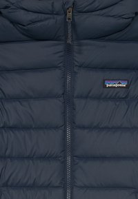 Veste matelassée bleu marine avec une fermeture éclair sur toute la longueur et des compartiments cousus. Présente le logo Patagonia sur le côté gauche. Texture lisse.