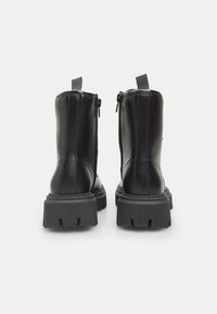 Botas negras de cuero hasta el tobillo con suela de goma gruesa, cremalleras laterales y acentos de tela en la parte superior. Incluye un lazo para facilitar su uso.