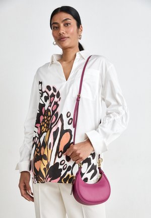 Chemise blanche avec un motif de papillons colorés, à manches longues, et une poche ; assortie à un petit sac à main en cuir violet arrondi.