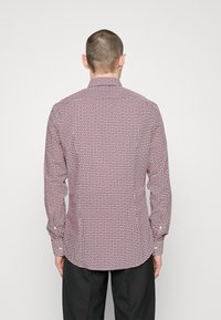 Pitkähihainen paita, jossa on punavalkoinen geometrinen kuvio, napilliset kalvosimet ja terävä kaulus, valmistettu kevyestä kankaasta.