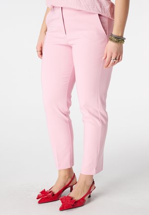 Pantalon rose tailleur en tissu lisse, coupe slim avec plis avant. Associé à des escarpins rouges brillants ornés de nœuds.