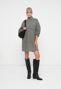 Grå strikket kjole med høy krage, ballongsikter og ribbet kant. Kombinert med svarte knelengde hælboots og en liten svart veske.