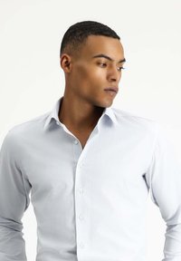 Camicia azzurro chiaro con bottoni, realizzata in tessuto liscio, con colletto a punta e maniche lunghe con polsini abbottonati.