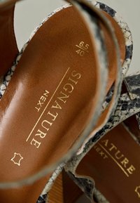 Sandali in pelle a scivolo con un motivo a serpente bianco e nero, suola interna marrone con branding dorato, taglia indicata come 6.5/40.