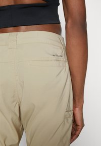 Helle beigefarbene Hose mit glatter Textur, ausgestattet mit einer Gesäßtasche und gestickten Details, versehen mit einem kleinen Columbia-Logo.