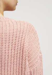 Hellrosa gestrickter Pullover mit strukturiertem Muster, lockerem Stich und lässiger Passform, der den Rücken und den Schulterbereich zeigt.