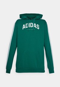 Grön bomullshoodie med en känguruficka, vitt adidas-logotyp och vita sidostråk längs ärmarna. Huva med dragsnören ingår.