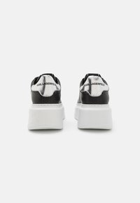 Sorte lærersneakers med en tykk hvit såle, metalliske detaljer og en logo bak. Glatt tekstur med rund form.