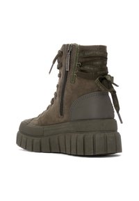 Zapatilla alta de ante verde con una suela gruesa y estriada, cremallera lateral y cordones decorativos en el tobillo. Elementos destacados incluyen goma texturizada y detalles cosidos.