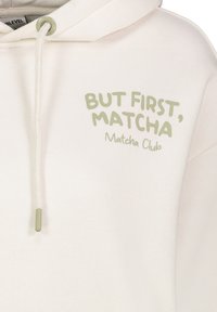 Crème hoodie met de tekst "Maar Eerst, Matcha Club" in het groen, met een trekkoordkap en van zachte katoen.