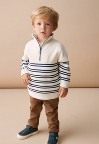 Suéter de punto a rayas blancas y azul marino con cuello de cremallera, combinado con pantalones caqui y zapatillas azul oscuro. Textura suave, corte relajado.