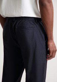 Marineblå bukser med elastisk midje, subtil tekstur, to baklommer, og et minimalistisk design. Mykt stoff med glatt finish.