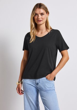 T-shirt noir à manches courtes avec un col rond, texture douce, coupe décontractée, associé à un jean bleu clair et un bracelet en or au poignet.